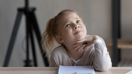 Thoughtful little kid girl looking up in distance, considering difficult school task, serious busy little female pupil studying, feeling stressed preparing assignments, homeschooling education conceptの写真素材
