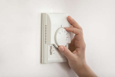Climate control. Close up of young woman hand switch on temperature regulator on wall mounted panel...