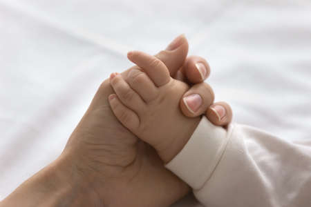 Young mom touching little palm of little baby. Mother holding cute hand of infant son or daughter in...