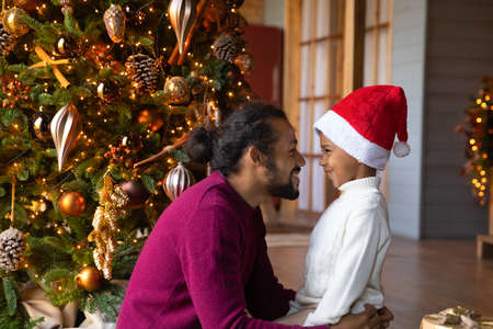 Smiling African American father and small son play enjoy New Year eve at home together. Happy biracial dad and boy child near fir tree relax on Christmas morning. Winter holiday celebration concept.の写真素材