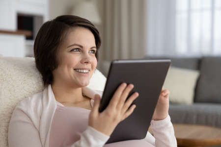 On maternity leave. Positive young pregnant lady sit in chair enjoy using electronic pad read ebook...