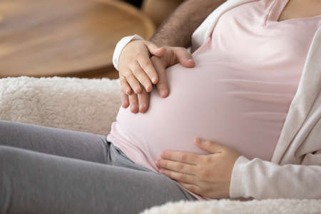 Dream come true. Cropped close up of happy couple of future parents embrace big belly with love care unity in parenthood. Expectant mom and dad holding hands on pregnant tummy happy to feel baby kicksの写真素材