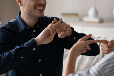 Close up cropped image smiling young deaf dumb family couple using sign language for communication. Happy millennial man and woman with hearing disability showing gestures, expressing feelings.の写真素材