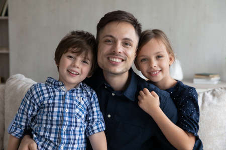 Portrait of affectionate loving young latin father posing at home with cute small children showing tender feelings. Happy multigenerational family looking at camera, holding video call conversation.の写真素材