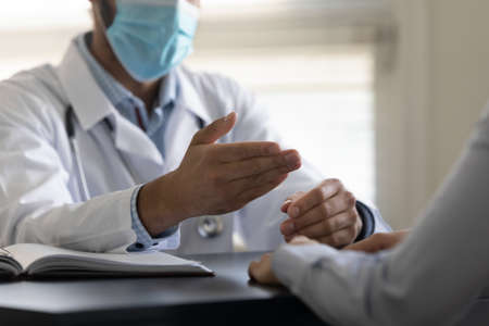 Hands of general practitioner in facemask speaking at appointment, meeting with patient during pandemic, giving consultation, gesturing. Medic care on epidemic concept. Low angle, close upの写真素材