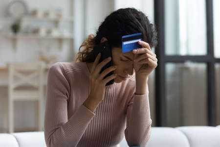 Unhappy millennial Caucasian female talk speak on cellphone with bank distressed with credit card...