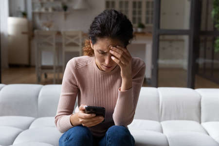 Unhappy young Caucasian woman look at cellphone screen distressed with bad message or news online....