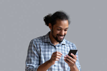 Head shot excited African American man using smartphone standing isolated on grey studio wall...