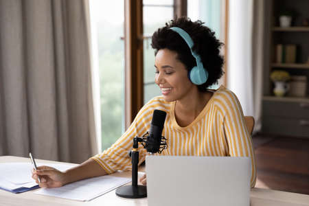 Smiling millennial african american woman radio program host or blogger in headphones recording...
