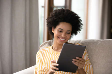Happy millennial generation african ethnicity woman holding digital touchpad gadget in hands,...