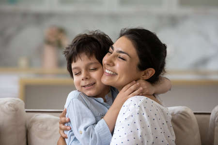 Sincere loving young asian indian woman cuddling cute little kid son, showing tender feelings. Happy two generations mixed race family enjoying sweet weekend moment together, relaxing at home.の写真素材
