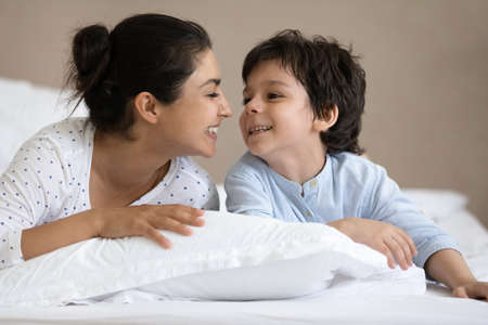 Head shot young happy indian ethnicity mother communicating with joyful cute small preschool child son on bed. Laughing two generations indian family playing spending leisure time in bedroom.の写真素材