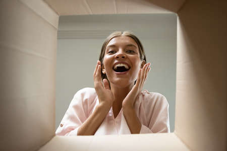Happy excited customer opening parcel, looking inside package with shock, surprise, joy. Smiling...