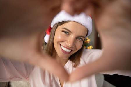Happy excited young Xmas girl looking at camera through hand heart frame, posing for romantic dating photo, smiling, enjoying Christmas party, celebrating New Year, expressing love, tendernessの写真素材