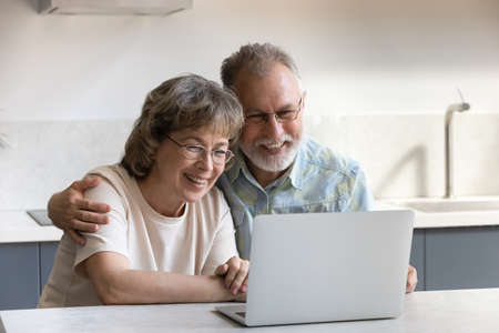 Happy bonding mature elderly couple using computer, shopping online choosing goods in internet store, communicating distantly with friends or grown children in social networks or holding video call.の写真素材
