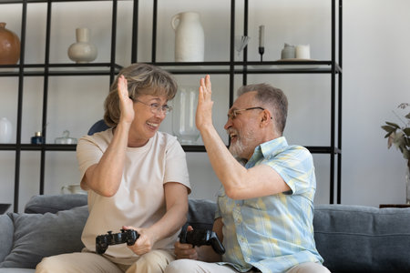 Happy candid older senior family couple giving high five, celebrating winning online video game. Emotional laughing middle aged man woman enjoying leisure activity, pensioners and modern technology.の写真素材