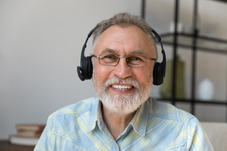 Happy old 60s man in headphones with microphone looking at camera starting online video call conversation, communicating distantly with friends or family, older people and modern technology concept.の写真素材