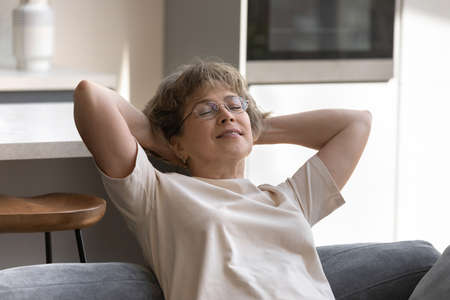 Happy relaxed middle aged senior retired woman in eyeglasses sleeping meditating on cozy sofa with...
