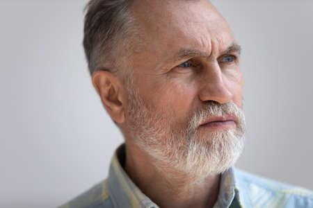 Close up head shot thoughtful middle aged 60s man looking in distance, suffering from psychological problems. Unhappy pensive old senior grandfather feeling lonely, isolate on white studio background.の写真素材