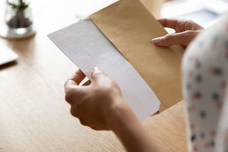 Hands of woman receiving letter, invitation, notification, postcard, taking out document for reading, opening envelope with blank folded paper at work desk. Mail concept. Close up, cropped shotの写真素材