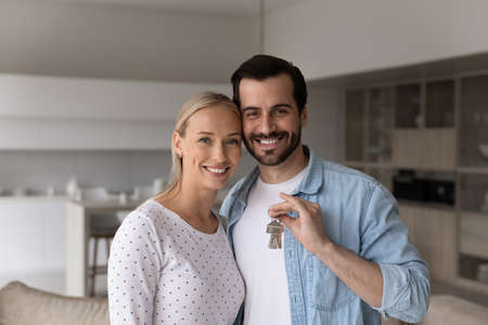 Portrait of smiling young family couple showing keys, feeling excited of moving into own stylish apartment, satisfied with professional real estate services. celebrating purchasing new dwelling.の写真素材