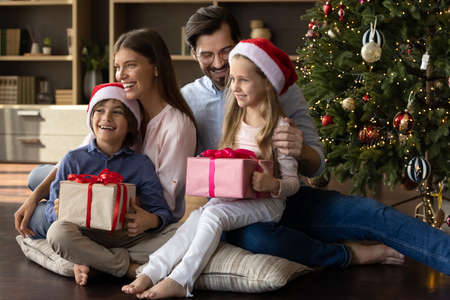Happy bonding young family couple sitting on pillows on floor in living room with laughing little...