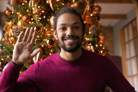 Portrait of smiling young African American man wave greet talk speak on video call on winter...