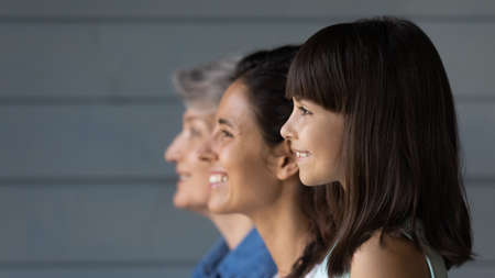 Happy cute 7s girl standing in line with young mother and senior grandmother, looking forward,...