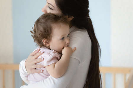 Close up loving mother hugging little daughter who biting fingers, family enjoying tender moment together, happy motherhood concept, caring young mom holding embracing adorable toddler child girlの写真素材