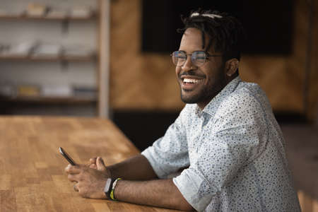 Happy dreamy young african american brazilian hipster man employee worker in eyeglasses holding...