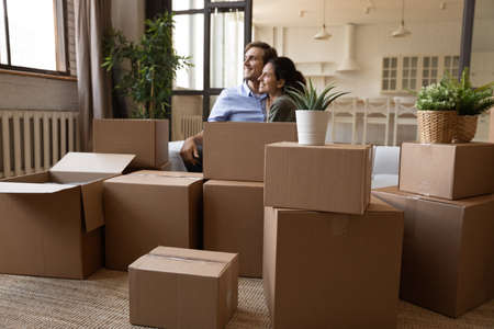 Young serene couple relaxing on sofa near heap of cardboard boxes with personal belongings on...