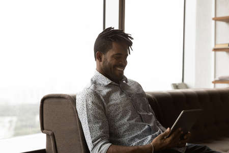 Happy young handsome African American Brazilian man using digital computer tablet, communicating...