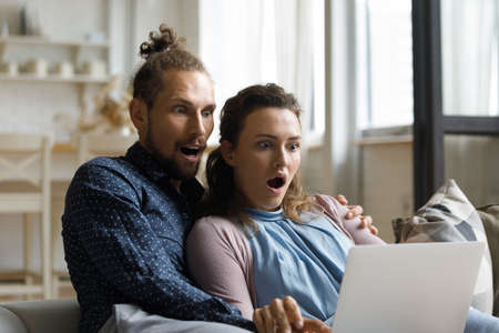 Shocked young bonding man woman family couple looking at laptop screen, reading email with...