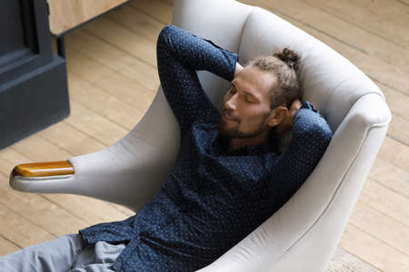 Above top view happy carefree millennial generation hipster man resting in cozy armchair with folded hands behind head, spending carefree leisure lazy weekend time alone at home, breathing fresh air.の写真素材