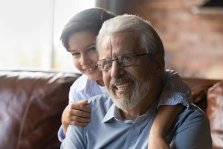 Best grandpa ever. Overjoyed little grandkid cuddle from back smiling mature grandfather in glasses. Loving preteen grandson enjoy kidding playing cute active game having fun together with grandparentの写真素材