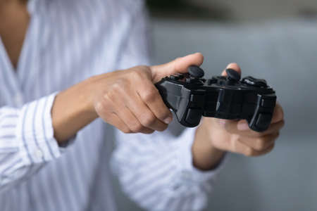 Cropped close up African American woman using gamepad, playing video game online, engaged in virtual...