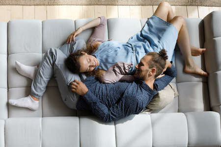 Top above full length view carefree happy millennial bonding man woman family couple lying on huge cozy sofa, enjoying trustful conversation, daydreaming napping, spending stress free weekend at home.の写真素材