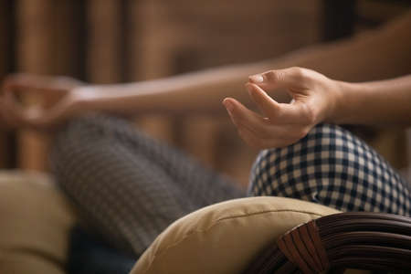 Mudra hand. Close up of young female practice meditation zen sit in pillows at home alone in lotus position. Millennial woman yogi engaged in spiritual practice. Focus on fingers joined in jnana signの写真素材