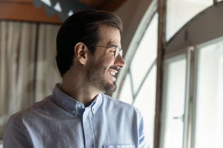 Head shot joyful young businessman manager employee in eyewear looking in distance out of window, feeling excited of new career opportunities, considering challenges, professional motivation concept.の写真素材