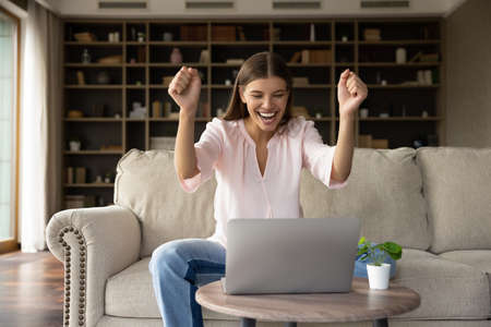 Euphoric young woman making yes gesture reading email with amazing news on computer, feeling joyful winning online lottery giveaway gambling betting auction prize or celebrating passing exams.の写真素材
