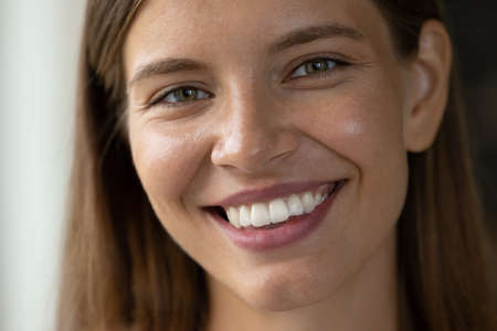 Close up head shot beautiful young woman with perfect skin looking at camera, showing whitening...