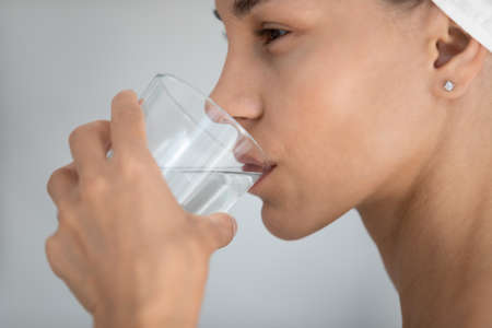 Cropped close up side view happy young mixed race latina woman drinking glass of fresh pure water, hydrating organism after morning shower, enjoying daily healthcare habit, preventing dehydration.の写真素材