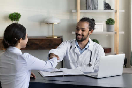 Smiling African American man doctor in white uniform with stethoscope and Indian patient client...