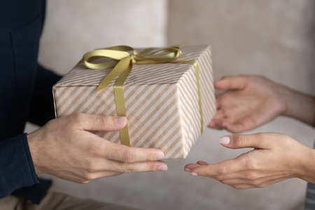Holiday celebration, family life event, anniversary, make surprise concept. Close up male hands giving long-awaited gift to sweetheart wife, congrats her on birthday, enjoy moment of receiving giftboxの写真素材