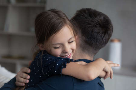 Little girl tightly cuddling her beloved daddy, close up. Young dad enjoy moment of tenderness and caress embracing his adorable daughter. Happy Father Day congratulations and family bonding conceptの写真素材