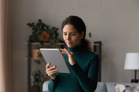 Using tablet pc. Confident user young latin female scroll web pages on wide screen of pad device...