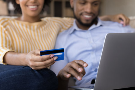 Young mix raced married couple shopping online from home, paying by credit card, making payments for purchase from virtual account, electronic wallet, paying bills, using laptop computer. Close upの写真素材