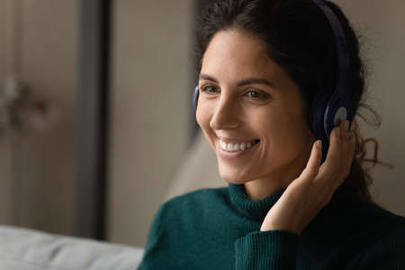 Digital headphones. Close up shot of smiling young latina woman wearing modern wireless earphones talking to customer online by video call. Skilled female interpreter translate virtual event remotelyの写真素材