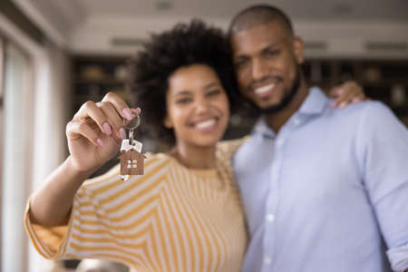 Happy Black millennial couple showing keys, smiling at camera, hugging. Husband and wife, new...