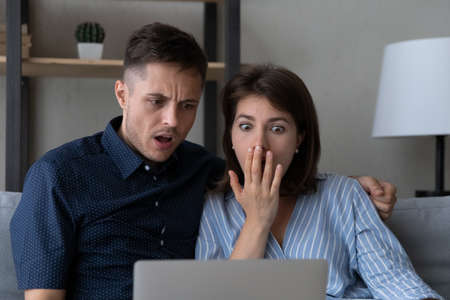 Shocked frustrated couple getting bad unexpected surprising news, staring at laptop screen, reading email message, notification, finding fraud, scam, financial data stealing, money lossの写真素材